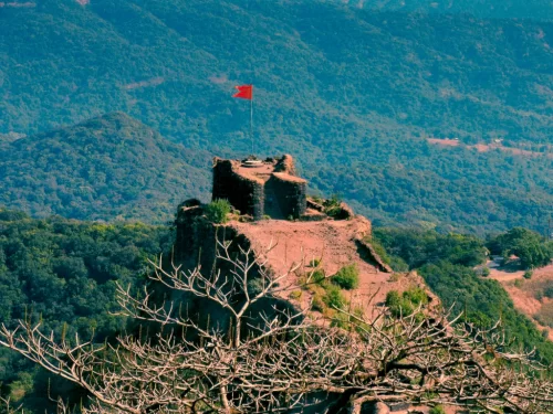 Pratapgad Fort Mahabaleshwar panoramic view, featuring ruined ramparts red saffron flag atop rocky peak surrounded lush misty Sahyadri mountains, perfect Maharashtra tour packages.