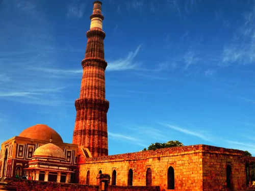Qutub Minar with Quwwat-ul-Islam Mosque and surrounding sandstone ruins under a vivid blue sky in Delhi, showcasing UNESCO World Heritage Indo-Islamic architecture for Qutub Minar tour packages.