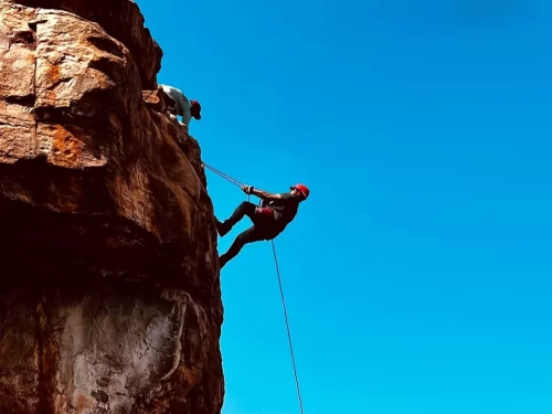 Rappelling adventure as climber descends a steep rocky cliff using safety ropes and harness.