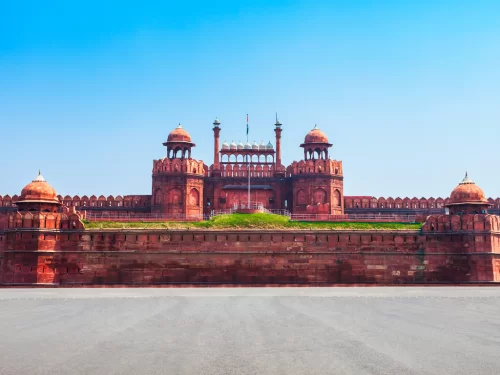 Red Fort main gate at Delhi on sunny day, featuring Indian flag and red sandstone towers, perfect heritage Delhi tour package. 