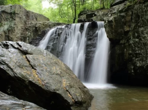 Rehala Falls near Manali featuring cascading waterfall over rocky cliffs surrounded by lush green forest.