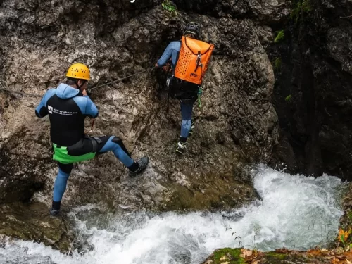River Canyoning adventure with climbers navigating rocky gorge beside rushing waterfall.