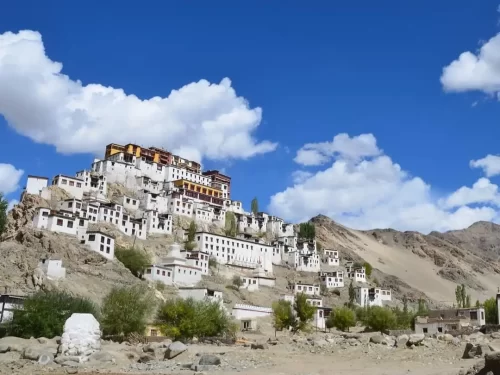 Rizong Gompa (Rizong Monastery) cascading white buildings with golden roofs on Ladakh hillside amid rocky slopes under blue sky with clouds, perfect Ladakh tour package.