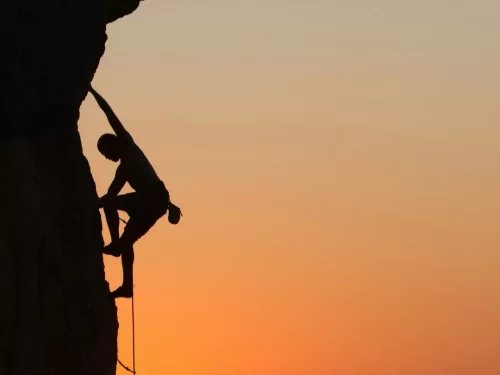 Rock Climbing silhouette of climber scaling steep cliff face against dramatic sunset sky.