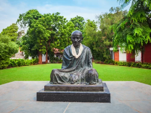 Gandhi statue at Sabarmati Ashram Ahmedabad during daylight, featuring lush gardens and trees, perfect cultural Gujarat tour package.