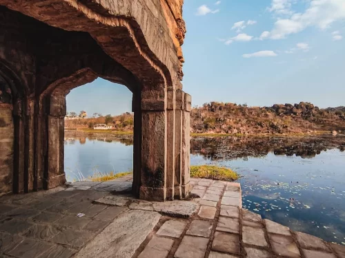 Stone pavilion overlooking Sangram Sagar Lake in Gwalior with calm waters and rocky hills in the background, a scenic heritage spot included in Madhya Pradesh tour packages