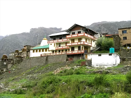 Shashur Monastery Keylong during overcast skies, featuring multi-story temple white dome green roof village homes stone wall mountains greenery, perfect spiritual experience Himachal Pradesh tour package.