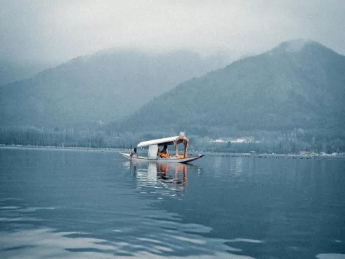 Shikara Ride traditional wooden boat gliding peacefully across a serene lake with misty mountains in the background.