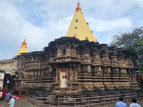 Shree Ambabai Mahalaxmi Temple in Kolhapur, Maharashtra, featuring detailed stone carvings and a tall yellow shikhara, a revered pilgrimage site included in Maharashtra tour packages.