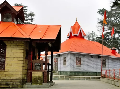 Shree Hanuman Temple Jakhu Shimla during misty weather, featuring orange roofs, deodar trees, flags, perfect spiritual adventure, Himachal Pradesh tour packages.