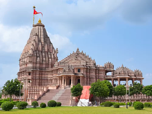 Shree Khodaldham Temple at Kagvad Rajkot during sunny partly cloudy day, featuring towering shikhara, saffron flag, intricate carvings and lush gardens, perfect spiritual experience with Gujarat tour packages.