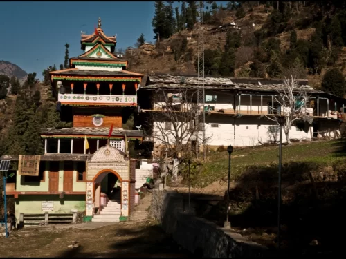 Shringa Rishi Temple in Jibhi featuring a traditional multi-tiered wooden Himachali temple with colorful carvings, arched entrance, and hillside backdrop surrounded by pine trees and village houses.