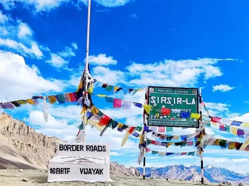 Sirsir La Pass BRO sign Project Viyayak 16BRTF Ladakh blue sky clouds, colorful prayer flags rocky arid mountains; perfect Spiti Valley Ladakh adventure tour package.