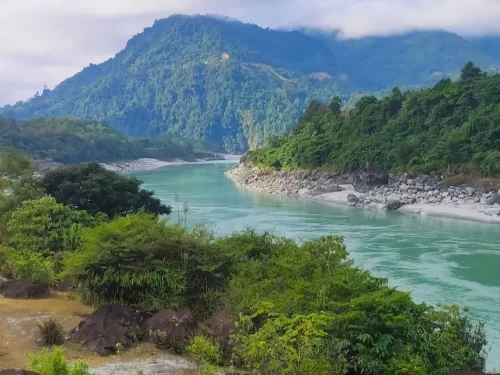 Siang Riverfront scenic turquoise river flowing through lush green hills and rocky banks in Arunachal Pradesh Tour Package.