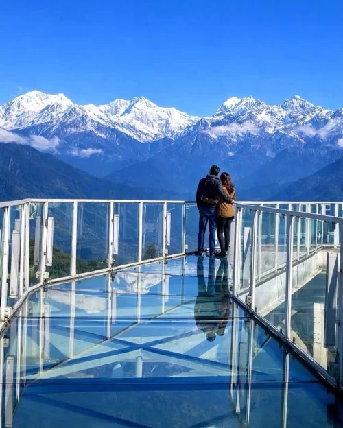 Couple standing on Pelling Skywalk in Sikkim with panoramic Kanchenjunga mountain views, a romantic highlight in Sikkim tour packages