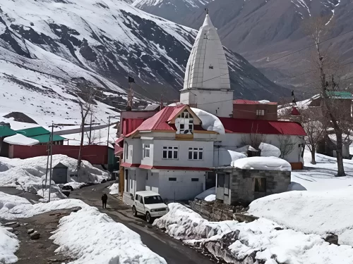 Sissu Raja Ghepan Temple snowy Lahaul village red roof white shikhara temple complex parked white SUV local walking snow-covered road majestic snow-capped peaks backdrop, perfect Himachal tour packages.
