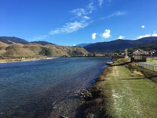 Siyom River crystal clear waters flowing beside grassy banks and scenic mountains in Arunachal Pradesh Tour Package.