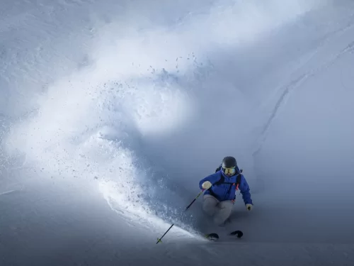 Skiing adventure with a skier carving through deep powder snow on a mountain slope, creating a dramatic spray of snow.