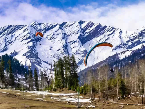Paragliding at Solang Valley Manali during partly cloudy skies, featuring colorful gliders over snow peaks pine forests and meadows, perfect adventure experience Himachal Pradesh tour package.