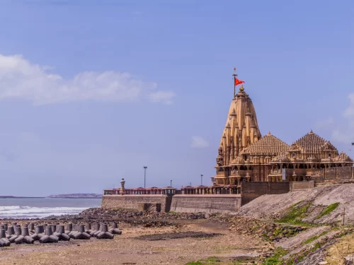 Shree Somnath Jyotirlinga Temple at Somnath Beach during clear day, featuring shikhara with saffron flag, sea waves, breakwaters, perfect pilgrimage experience with Gujarat tour packages.