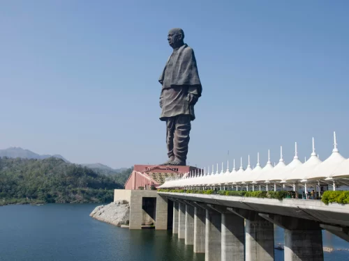 Statue of Unity in Gujarat during clear day, featuring 182m tall Sardar Patel bronze statue, connecting bridge with white canopies, Narmada River and surrounding hills, perfect cultural landmark with Gujarat tour packages.