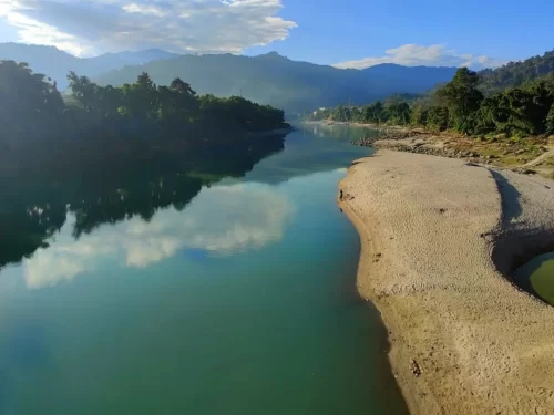 Subansiri River serene emerald waters flowing past sandy banks and forested hills in Arunachal Pradesh Tour Package.