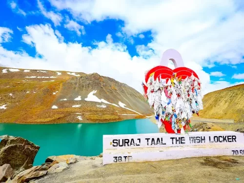 Suraj Tal Lahaul Spiti Himachal Pradesh India iconic red heart shaped wish locker signpost with colorful ribbons locks overlooking turquoise lake snowy brown mountains blue skies scattered clouds highway edge, perfect Manali Leh highway romantic tour pack