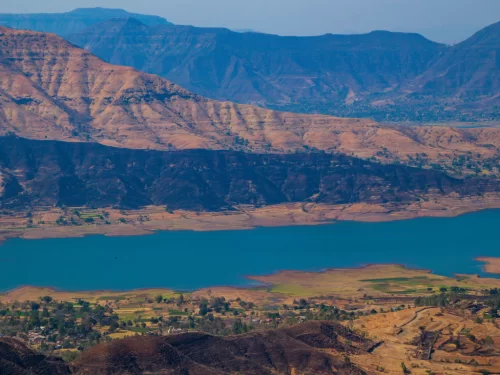 Sydney Point Panchgani during sunny weather, featuring Kate's Point lake, Sahyadri mountains, fields, perfect scenic adventure, Maharashtra tour packages. 