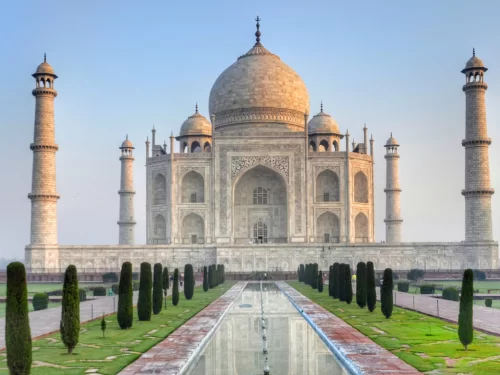 Classic Taj Mahal front view Agra Uttar Pradesh with reflecting pool, cypress trees, white marble mausoleum, four minarets, blue sky, perfect UNESCO heritage India tour package. 