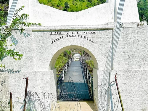 Teetwal Village Forest Department suspension bridge gate during sunny day Kashmir, featuring white arch J&K Forest Dept 1989 greenery wooden bridge barbed wire backdrop, perfect Kashmir tour packages. 