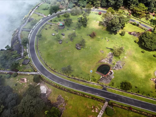 Thangkharang Park Cherrapunji during misty morning, featuring aerial view green lawns winding roads pavilion sacred pool trees lake backdrop, perfect nature park experience Cherrapunji Meghalaya tour package.