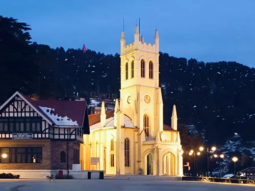 Christ Church at The Ridge Shimla during twilight winter, featuring illuminated Gothic spires clock tower snow pine hills half-timbered house lamps, perfect heritage cultural experience Himachal Pradesh tour packages.