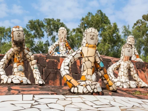 Colorful mosaic sculptures at Rock Garden Chandigarh during sunny day, featuring human figures, trees, rocky base, perfect cultural Himachal Pradesh tour package.