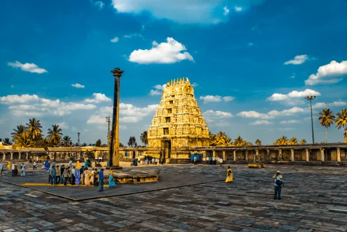 Chennakeshava Temple in Belur featuring a golden Rajagopuram tower, historic stone pillar, and paved courtyard, perfect heritage experience with Belur tour package.