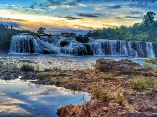Thlu Amwi Falls Meghalaya wide cascading waterfall with rocky riverbank and sunset sky view