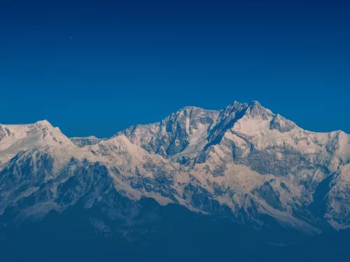 Snow-capped Kanchenjunga range from Tiger Hill in Darjeeling during clear morning, featuring blue sky and Himalayan peaks, perfect Sikkim tour package