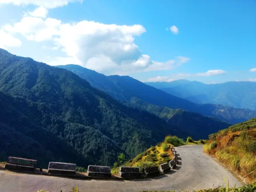 Mountain road to Tiger Hill in Darjeeling during sunny daytime, featuring winding road, green valleys and blue sky, perfect Sikkim tour package
