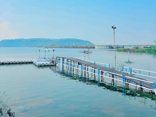  Tighra Dam in Gwalior with calm reservoir waters, floating jetty walkway, and dam structure against distant hills, a scenic getaway featured in Madhya Pradesh tour packages