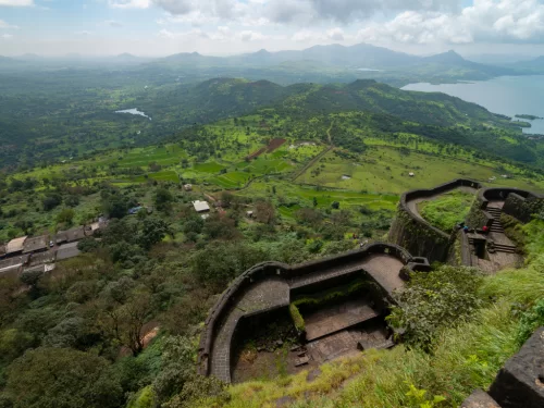 Tikona Fort Maharashtra panoramic green monsoon walls Pawna lake valleys, curved bastions villages Lohagad Korigad peaks Western Ghats, perfect Lonavala Maval forts trek package. 