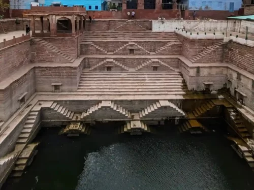 Toorji Ka Jhalra Jodhpur Ornate 18th-century stepwell featuring intricate rose-red sandstone carvings, symmetrical geometric staircases, and deep turquoise waters Rajasthan.