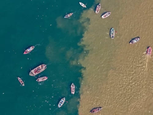Triveni Sangam aerial view, scattered white boats green brown rivers meeting, perfect Uttar Pradesh tour package.