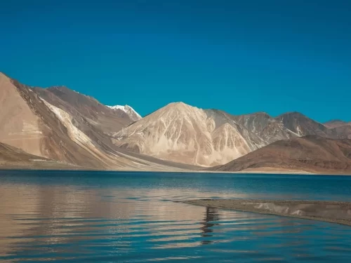 Scenic Tso Moriri Lake in Ladakh during clear day, featuring snow-capped Zanskar mountains reflections in turquoise waters, perfect adventure experience with Ladakh tour package.