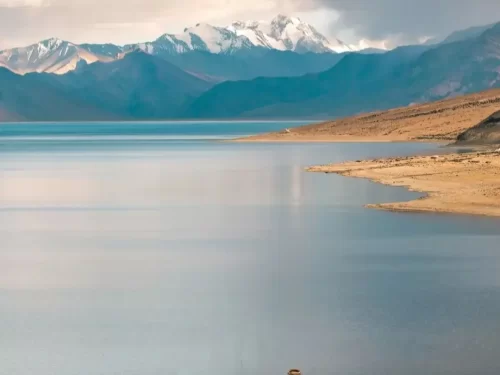 Tso Moriri Lake in Ladakh during cloudy skies, featuring snow-capped peaks reflections in turquoise waters and sandy shores, perfect adventure experience with Ladakh tour package. 