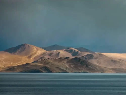 Tso Moriri Lake in Ladakh during dramatic cloudy skies, featuring barren rugged mountains and serene blue waters, perfect adventure experience with Ladakh tour package. 