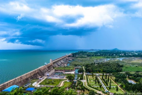 Tungabhadra Dam And Garden in Hosapete featuring expansive reservoir wall, manicured gardens, and dramatic cloudy sky, perfect sightseeing experience with Hampi tour package.