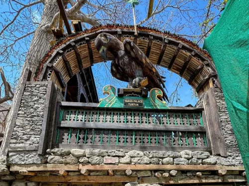 Ornate wooden eagle sculpture archway entrance at Turtuk village Nubra Ladakh with green signboard, stone walls and barren trees, perfect Balti cultural heritage gateway with Ladakh tour package.