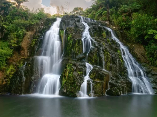 Tyrshi Falls majestic cascade at Jowai Meghalaya during cloudy day, featuring lush rainforest mossy rocks fern trees pool, perfect nature adventure Meghalaya tour package.