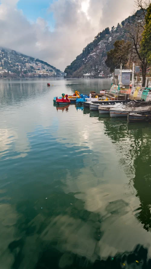 Nainital Lake scenic boating view with colorful paddle boats, hill town reflections, and misty mountains landscape in Uttarakhand tour packages