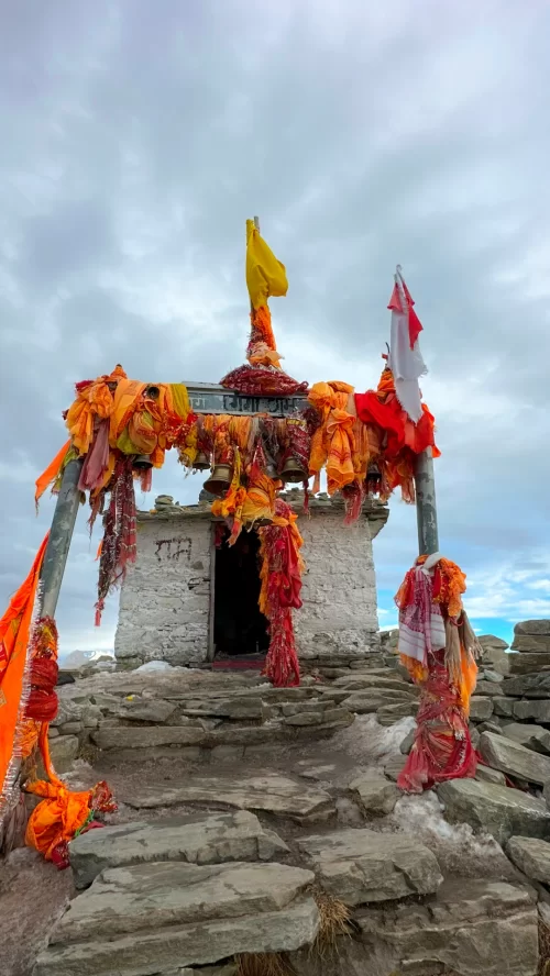A stone shrine at Tungnath in Chopta, adorned with saffron prayer cloths and brass bells, frequently visited by travelers on Uttarakhand tour packages.