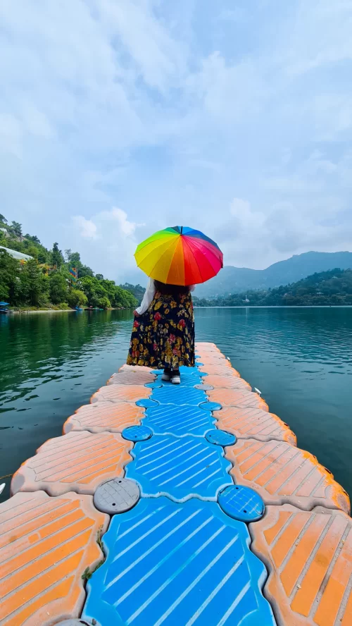 A serene floating bridge over the tranquil Bhimtal Lake, Uttarakhand, with a person holding a vibrant rainbow umbrella—perfect for peaceful retreats in Uttarakhand tour packages.